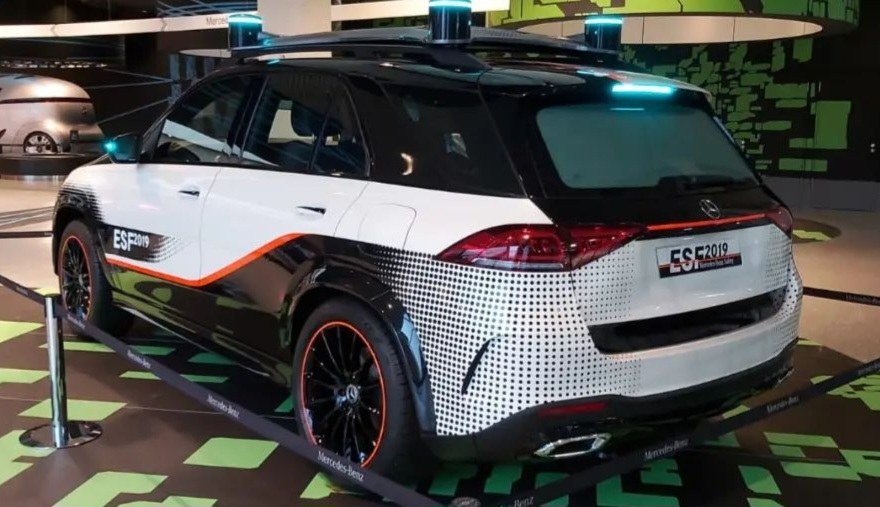 Mercedes-Benz E-Klasse Electric SUV auf der IAA in Frankfurt, umgeben von Absperrpollern mit Seilen und Lichtern, mit einem weiteren Fahrzeug und Text an der Wand im Hintergrund.