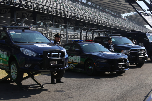 Polizeiautos vor einer Rennstrecke geparkt, im Hintergrund ein Stadion mit Geländern und Maschendrahtzaun.