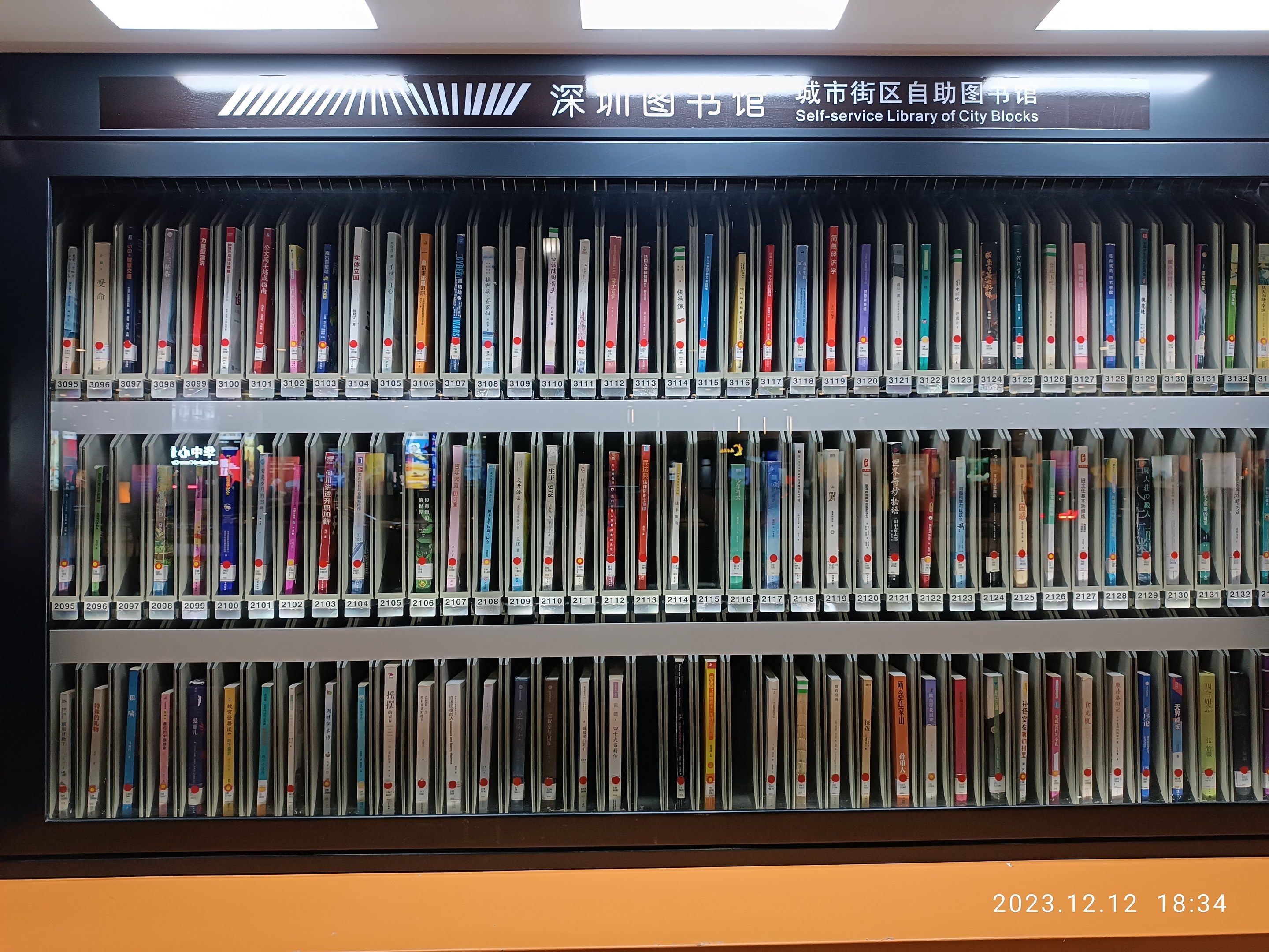 Eine gut beleuchtete Bibliothek mit hohen Bücherregalen voller Bücher, mit einer Tafel mit Text und einem Wasserzeichen unten, das an eine Selbstbedienungsbibliothek von Stadtblöcken erinnert.