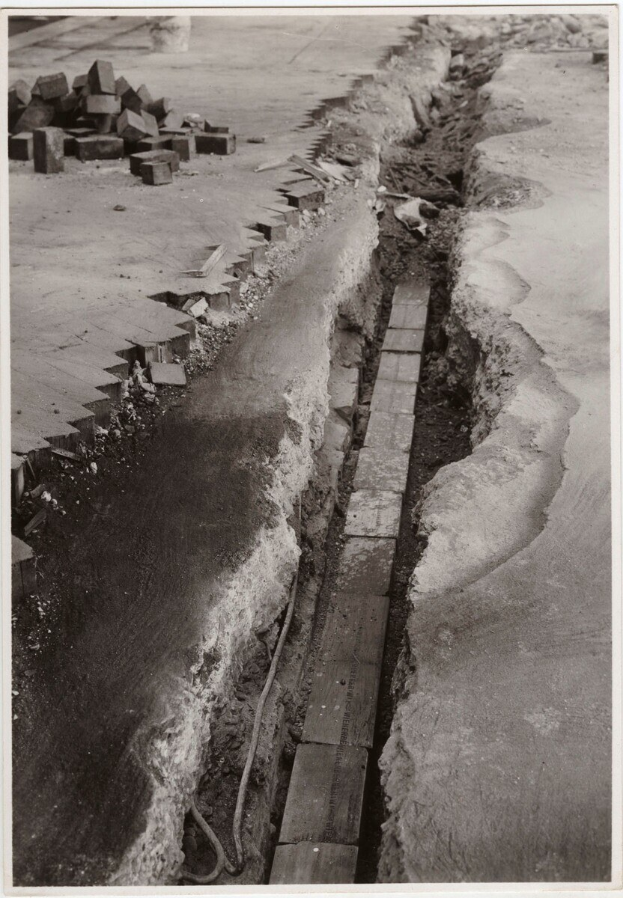 Ein Schwarz-Weiß-Foto einer gebrochenen Straße mit verstreuten Ziegeln auf der linken Seite.