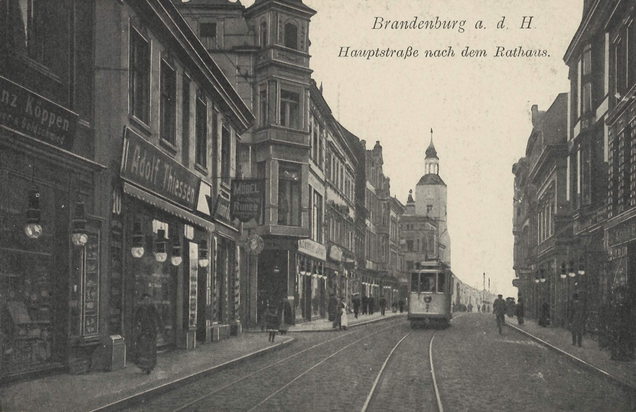 Schwarz-weiß-Foto einer Stadtstraße in Brandenburg, Deutschland mit einer Straßenbahn, Fußgängern, Gebäuden, Schildern, Straßenlaternen und einem bewölkten Himmel.