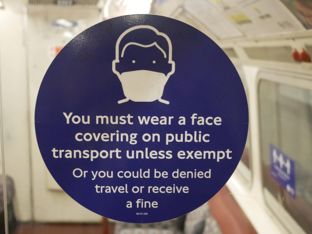 Schilder an einer Zugtür, das das Tragen von Gesichtsbedeckungen auf öffentlichen Verkehrsmitteln anzeigt, mit einem Glasfenster rechts.