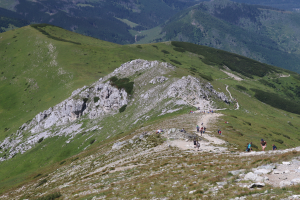 Gruppe von Menschen beim Wandern auf einem Berg mit grüner Wiese und felsigem Gelände, Himmel im Hintergrund sichtbar