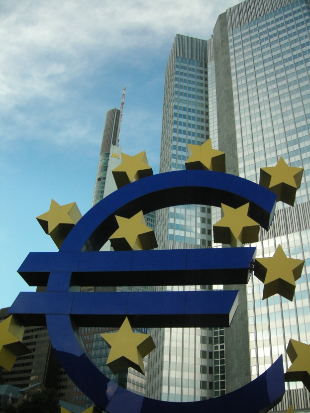 Euro-Zeichen vor dem Hauptsitz der Europäischen Zentralbank in Frankfurt, Deutschland, mit dem Gebäude umgeben von Bäumen unter einem bewölkten Himmel.