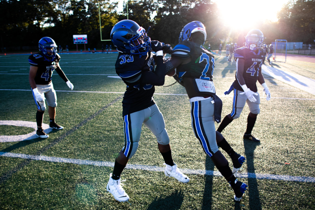 Gruppe junger Männer beim Fußballspielen auf einem Feld mit Bäumen und einem klaren blauen Himmel, mit Helmen und Schuhen.