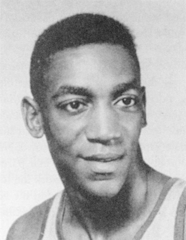 Ein Mann in einem weißen "Basketball Hall of Fame"-Trikot lächelt warmherzig, sein Haar ist zurückgekämmt und er strahlt Selbstbewusstsein aus.