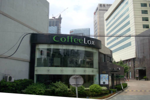 Ein Geschäftsgebäude mit ein paar Pflanzen davor, umgeben von vielen hohen Gebäuden und Stromleitungen.