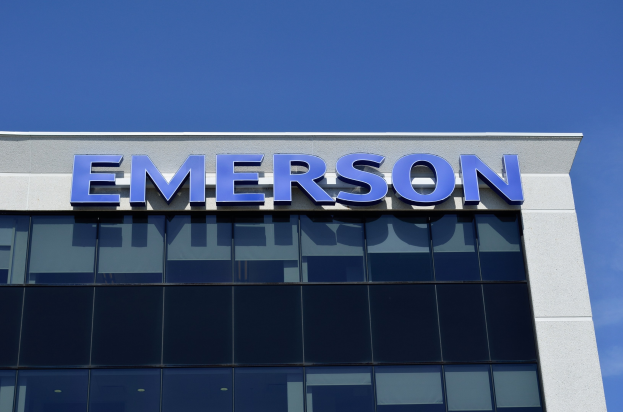 Emerson-Logo an einer Gebäudefassade mit dem Text "Emerson investiert 1,5 Milliarden USD in den USA" vor einem klaren blauen Himmel.