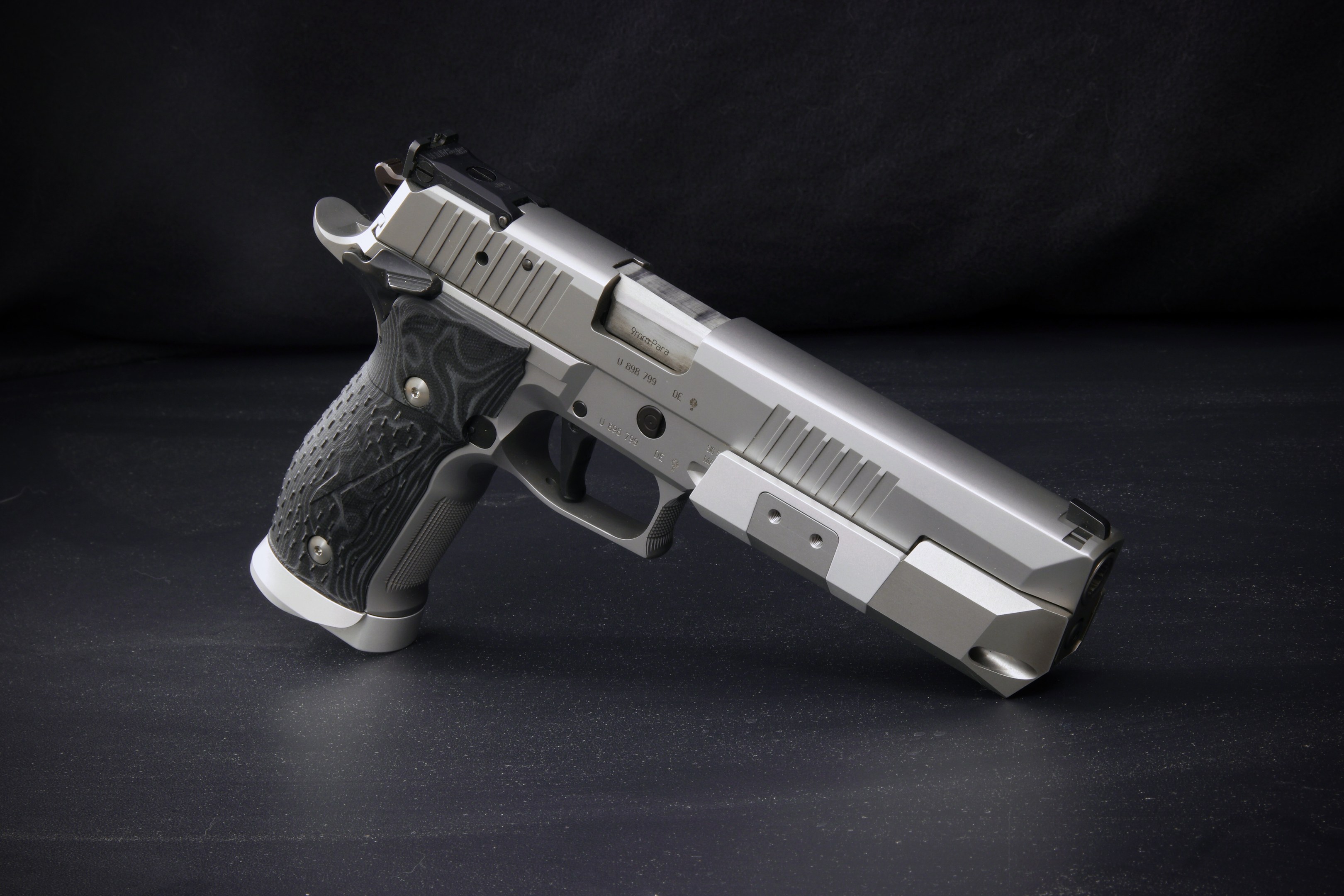 Eine Sig Sauer P226 X-Five 9mm Pistole auf einer schwarzen Oberfläche mit schwarzem Hintergrund.