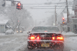 Eine schneebedeckte Straße mit spärlichem Verkehr, gesäumt von schneebedeckten Bäumen und Häusern auf beiden Seiten.