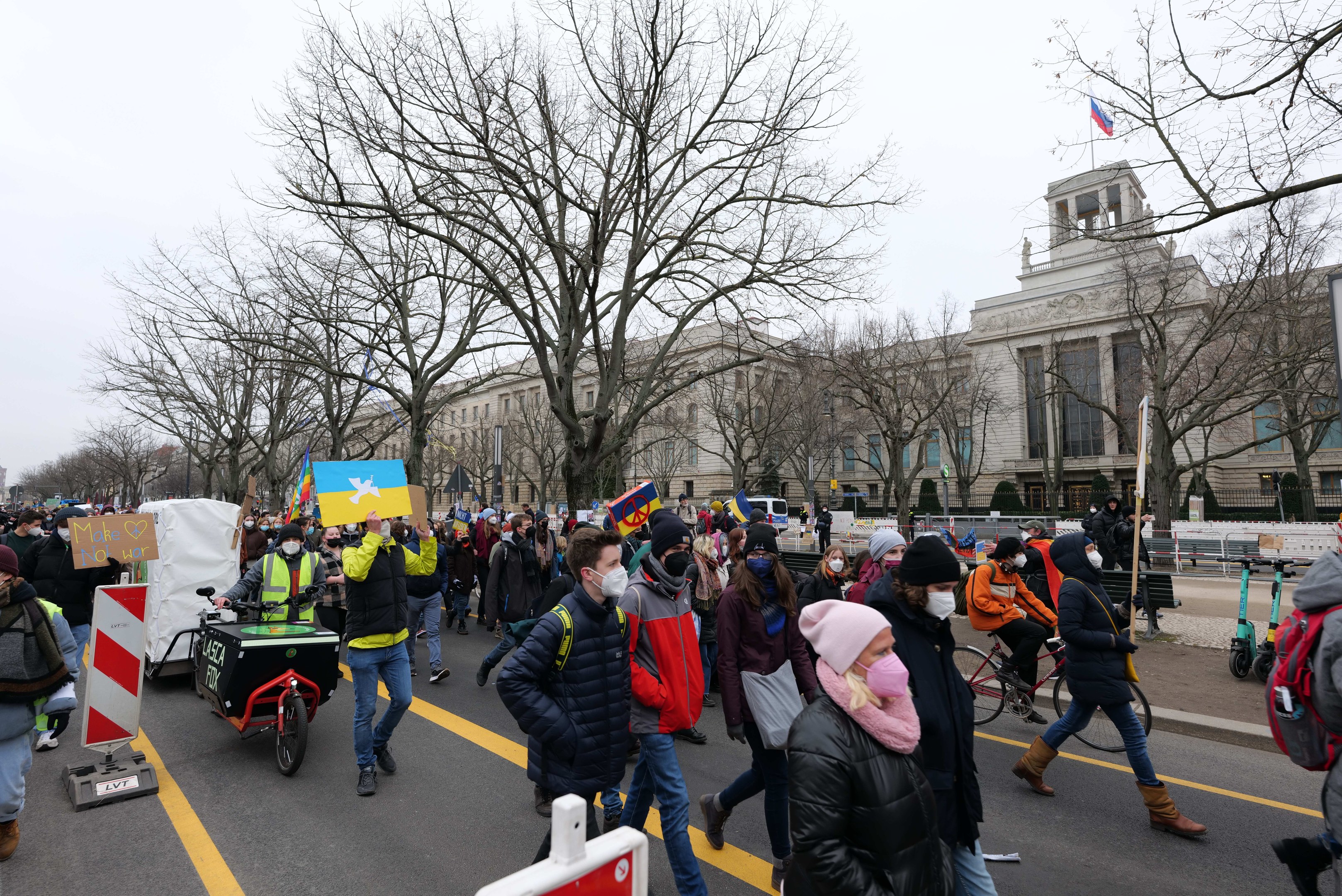 Eine große Gruppe von Menschen marschiert bei einer Demonstration auf einer Straße in Washington, D.C., mit Schildern und Bannern, einige fahren Fahrräder, unter einem klaren blauen Himmel.