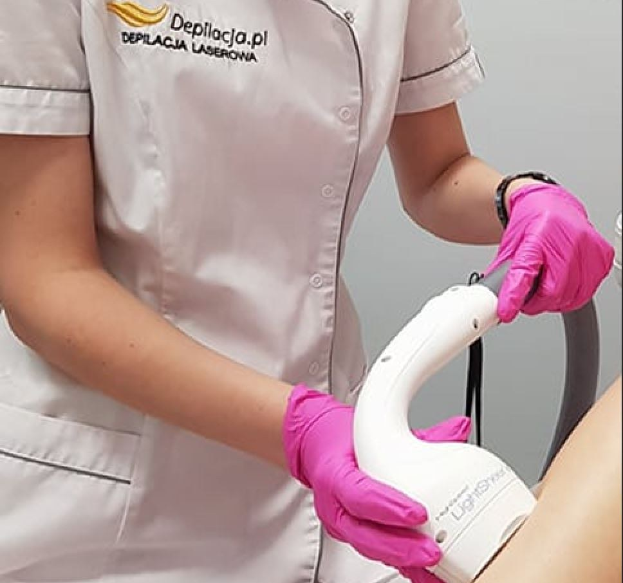 Eine Frau in einem weißen Hemd und pinken Handschuhen bedient eine weiße Laser-Haarentfernungsvorrichtung auf ihrer Haut, steht vor einer Wand.