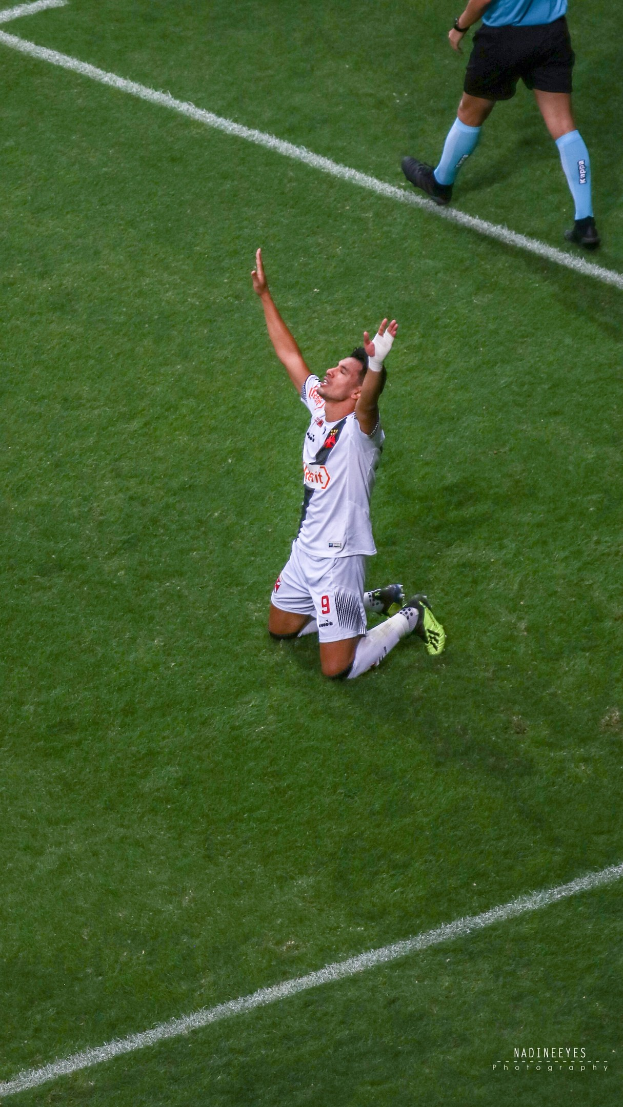 Ein Fußballspieler kniet auf dem Boden mit ausgestreckten Armen in Feierlaune, trägt einen Sportdress und Fußballschuhe.