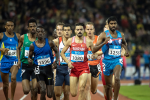 Eine Gruppe von Männern, die auf einer Bahn laufen und an einem Rennen teilnehmen, mit einigen, die zum Ziel sprinten, mit einem unscharfen Hintergrund.