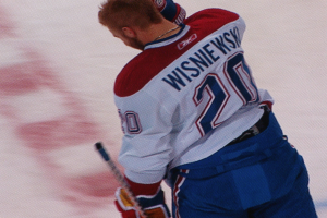 Ein Eishockeyspieler in einem "Wisniewski"-Trikot steht auf dem Eis und hält einen Eishockeyschläger in der Hand, mit einem konzentrierten und entschlossenen Gesichtsausdruck.