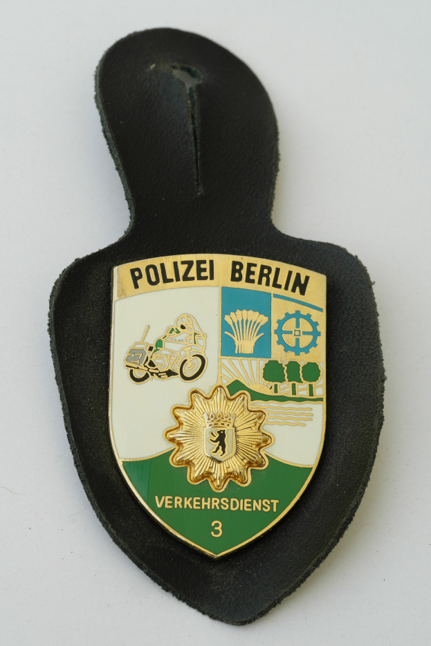 Ein Polizeistern mit der Aufschrift "Polizei Berlin" in fetter schwarzer Schrift auf einem blauen Schild mit einem weißen Stern und einem weißen Rand.