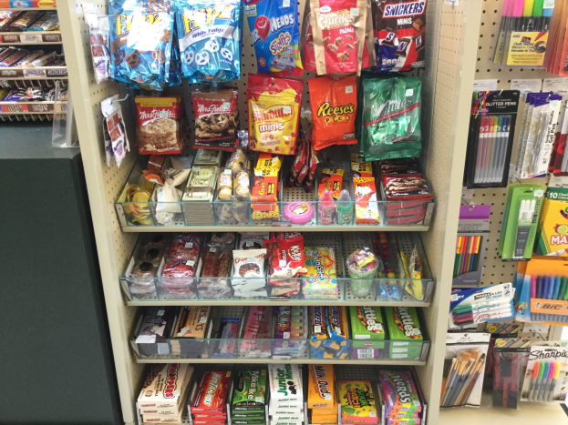 Ein Geschäft mit verschiedenen Arten von Süßigkeiten, darunter Pakete, Schachteln und Stifte, die auf Regalen angeordnet sind, mit einer Süßigkeitenauslage auf der linken Seite.