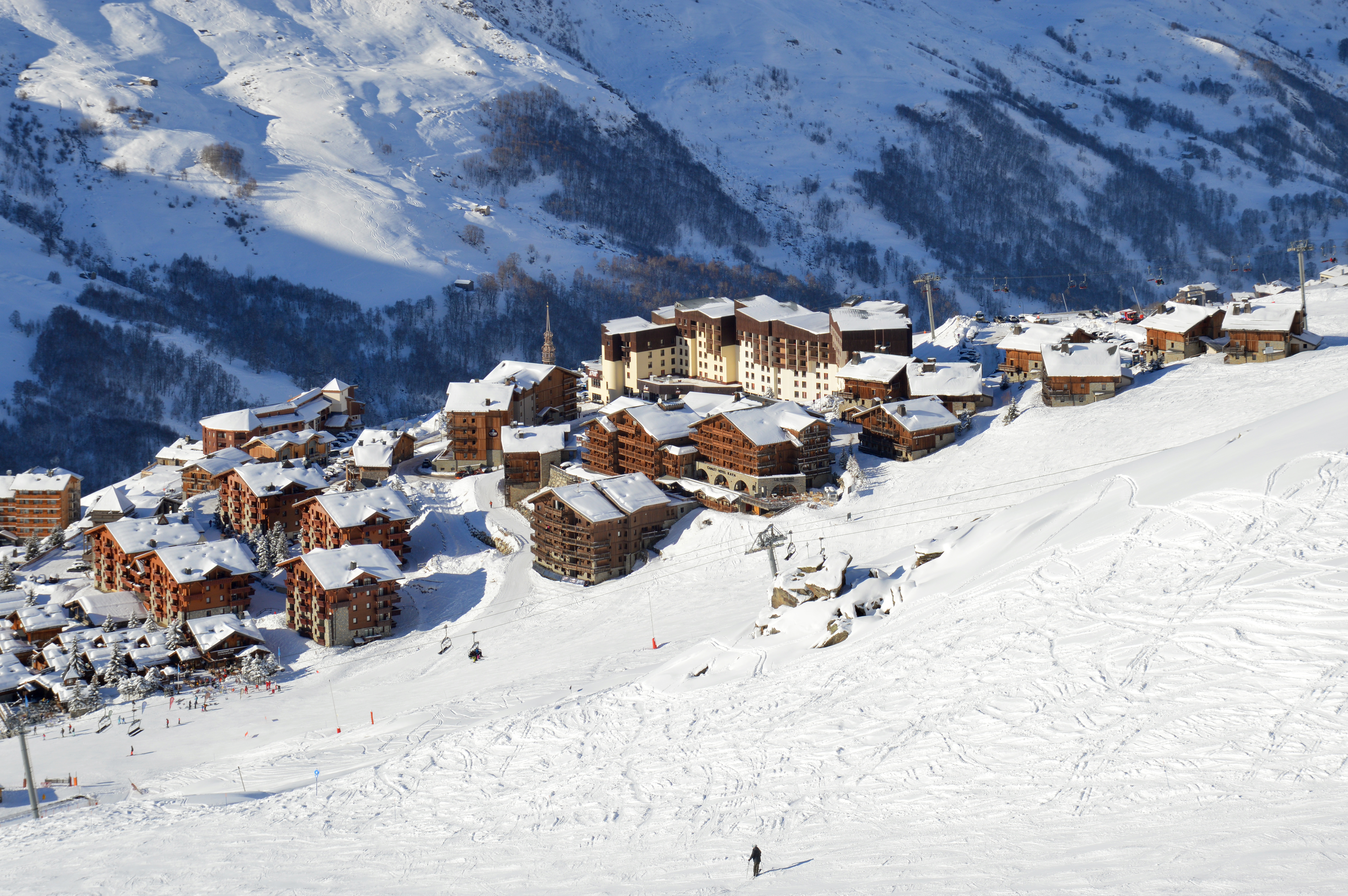 Ein Skigebiet in den französischen Alpen mit schneebedeckten Bergen, Gebäuden, Bäumen und Menschen, die die Pisten hinunterski