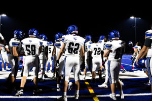 Eine Gruppe von Fussballspielern in Helmen und Stiefeln steht auf einem Feld, mit Flutlichtmasten im Hintergrund.