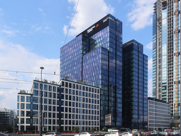 Hauptsitz der Deutschen Bank in Frankfurt, Deutschland, ein großes mehrstöckiges Gebäude mit zahlreichen Fenstern, umgeben von städtischer Infrastruktur wie Straßenlaternen, Elektrokabeln, Fahrzeugen und Grünflächen.