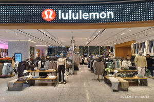 Das Innere eines lululemon-Ladens in Singapur mit Schaufensterpuppen in der neuesten Mode, Kleidung an Bügeln und Tischen mit verschiedenen Artikeln, alles beleuchtet von Deckenlampen und einem Namensschild mit Text, mit einem Wasserzeichen auf dem Bild.