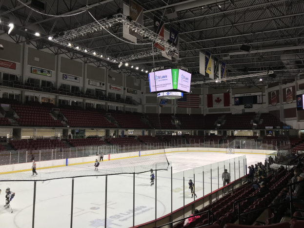 Eishockeyspiel in einer großen Arena mit einem zentralen Netz, Zuschauern auf beiden Seiten, Deckenbeleuchtung und Bannern, identifiziert als die St. Louis Blues Arena.