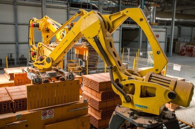 Großes Industrie-Hochregallager mit gestapelten Kisten, Kränen, Zaun, Pfählen und einer fernen Wand in einer Fertigungsumgebung.