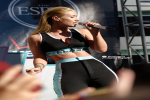 Eine Frau singt in ein Mikrofon mit einem Banner im Hintergrund.