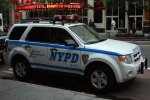 Ein weißes Auto steht am Straßenrand mit Geschäften mit Glastüren im Hintergrund.