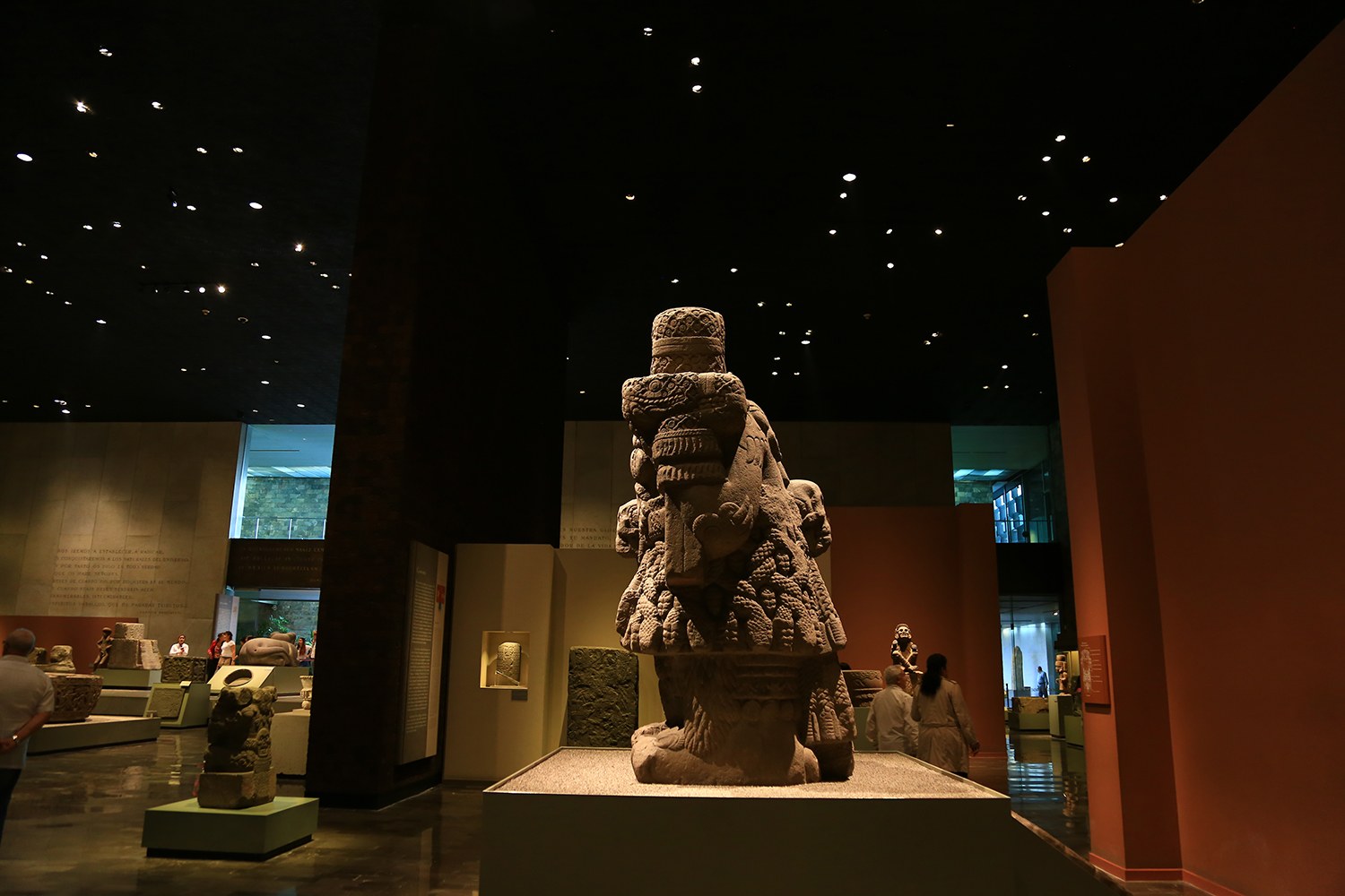 Eine Gruppe von Menschen in einem Museum, die Skulpturen auf Sockeln unter Deckenlampen betrachtet, mit Museumswänden im Hintergrund.