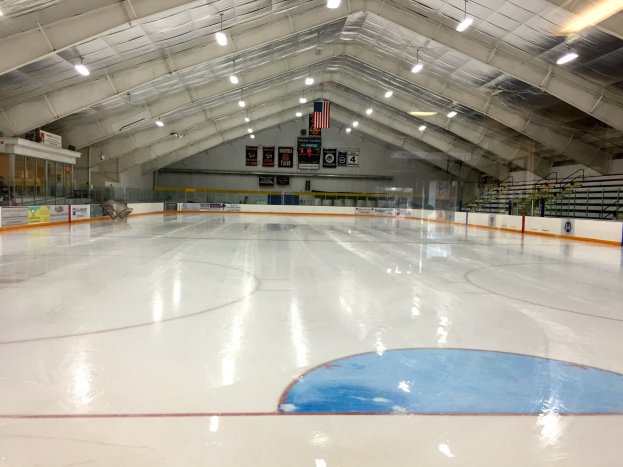 Großes Hallen-Eisstadion mit Deckenbeleuchtung, Werbetafeln, einer Wand, Treppen mit Geländern und einigen Menschen, wahrscheinlich eine Hockey-Anlage.