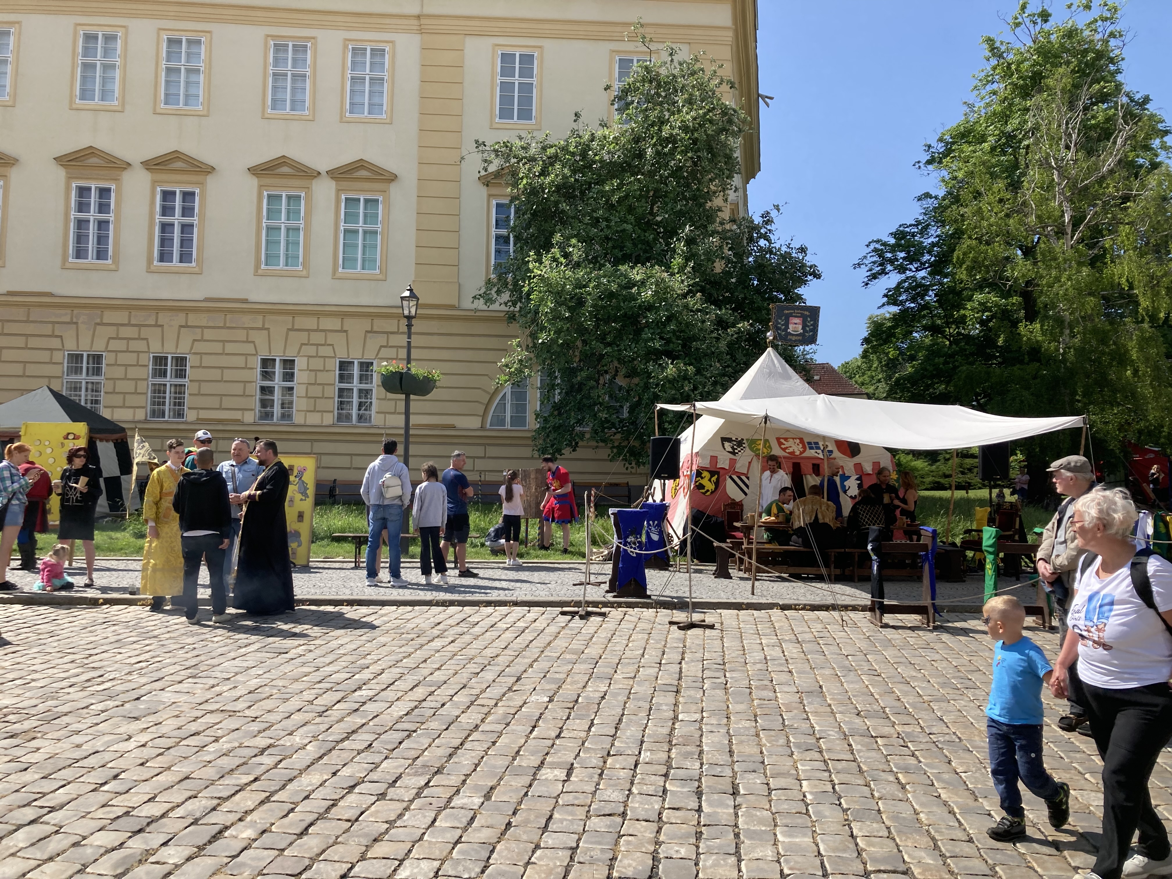 Eine Gruppe von Menschen geht eine Kopfsteinpflasterstraße in Krakau, Polen, entlang mit Zelten, Tischen und einem Gebäude mit sichtbarem Text im Hintergrund.