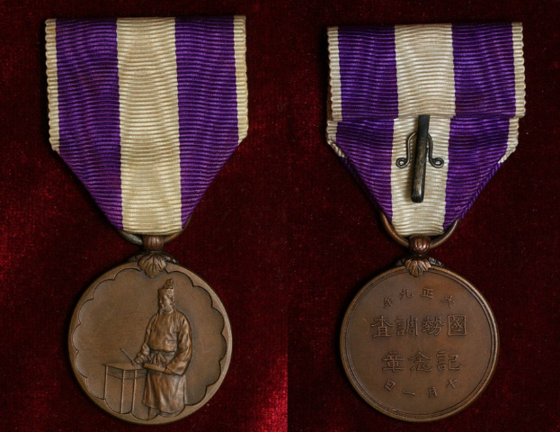 Zwei Medaillen mit lila und weißen Bändchen, mit eingravierter Schrift, auf einer maronenfarbenen Oberfläche.