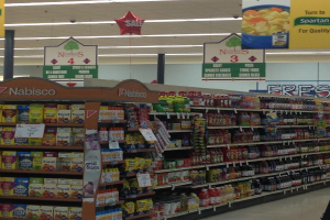 Ein Supermarkt-Innere mit Regalen voller Lebensmittel, Deckenleuchten und Schildern.