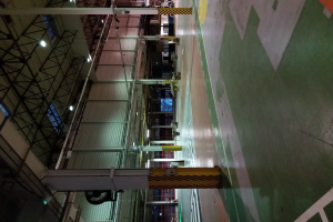 Eine große Lagerhalle voller verschiedener Maschinen, Metallstangen, Lampen und andere Gegenstände, mit sichtbarem Text auf dem Boden rechts.