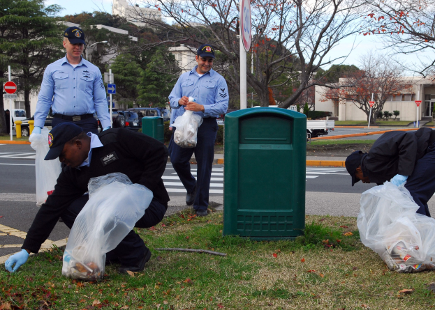 Drei Polizisten in Uniform sammeln Straßenmüll, während Fahrzeuge im Hintergrund vorbeifahren.
