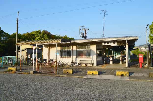 Fahrräder vor einem Bahnhof mit Häusern, Bäumen, Strommasten und Drähten im Hintergrund, einer Straße unten und einem klaren blauen Himmel.