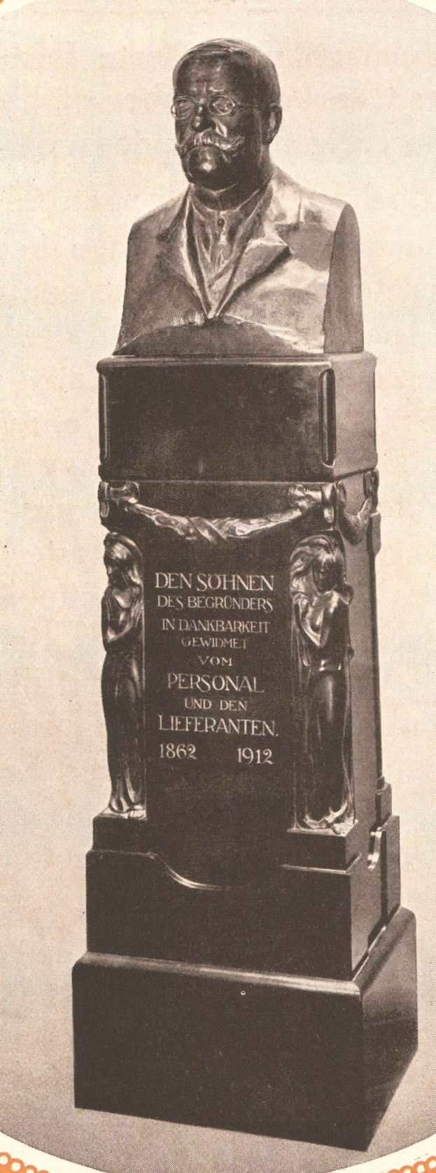 Schwarzes und weißes Foto einer Büste eines Mannes in Anzug und Krawatte, mit Gedenktext beschriftet, wahrscheinlich ein Denkmal.