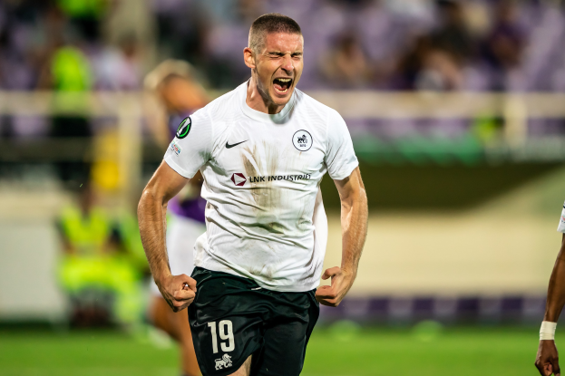 Ein Mann in weißem Hemd und schwarzen Shorts läuft auf einem Fußballfeld, umgeben von einer Gruppe von Menschen, die ein Tor in einem Spiel zwischen Leeds United und Melbourne Victory feiern.