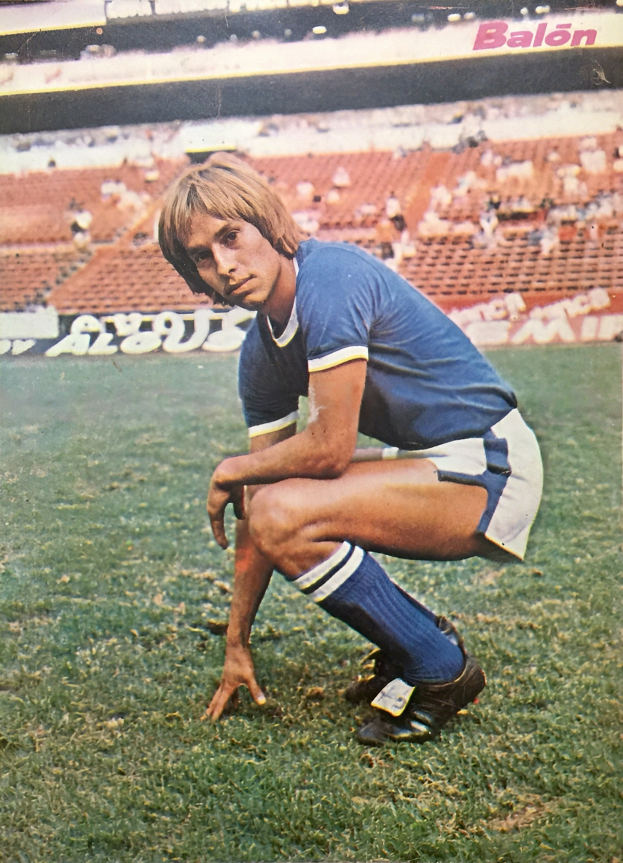 Ein Mann kniet auf einem Fußballfeld umgeben von sitzenden Personen mit Schildern.