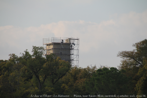 Ein Baugerüst in der Mitte des Bildes, mit Bäumen unten und einem Himmel oben, und Text in der unteren Ecke.