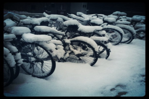 Mehrere Fahrräder stehen auf einem schneebedeckten Boden, wobei auch die Fahrräder mit Schnee bedeckt sind.