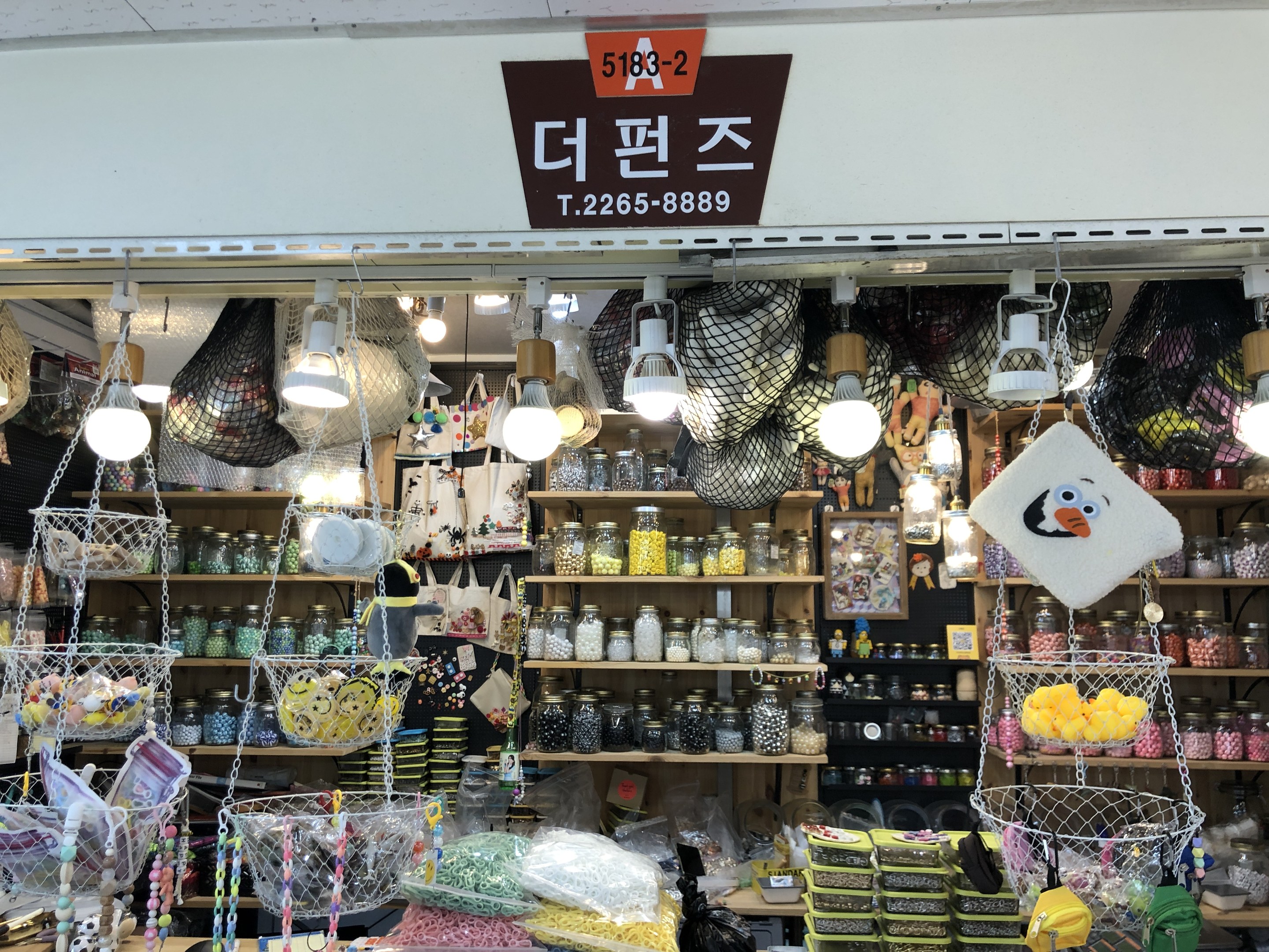 Ein unordentlicher Laden in Seoul mit verschiedenen Gegenständen wie Körbchen, Lichtern, Flaschen und Spielzeugen auf Regalen, mit einer Tafel öber der Tür, die anzeigt, dass es einer der besten koreanischen Läden ist.