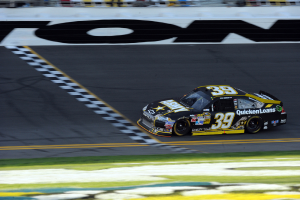 Ein Rennwagen auf einer Straße mit Gras am Boden, mit Text auf seiner Karosserie.