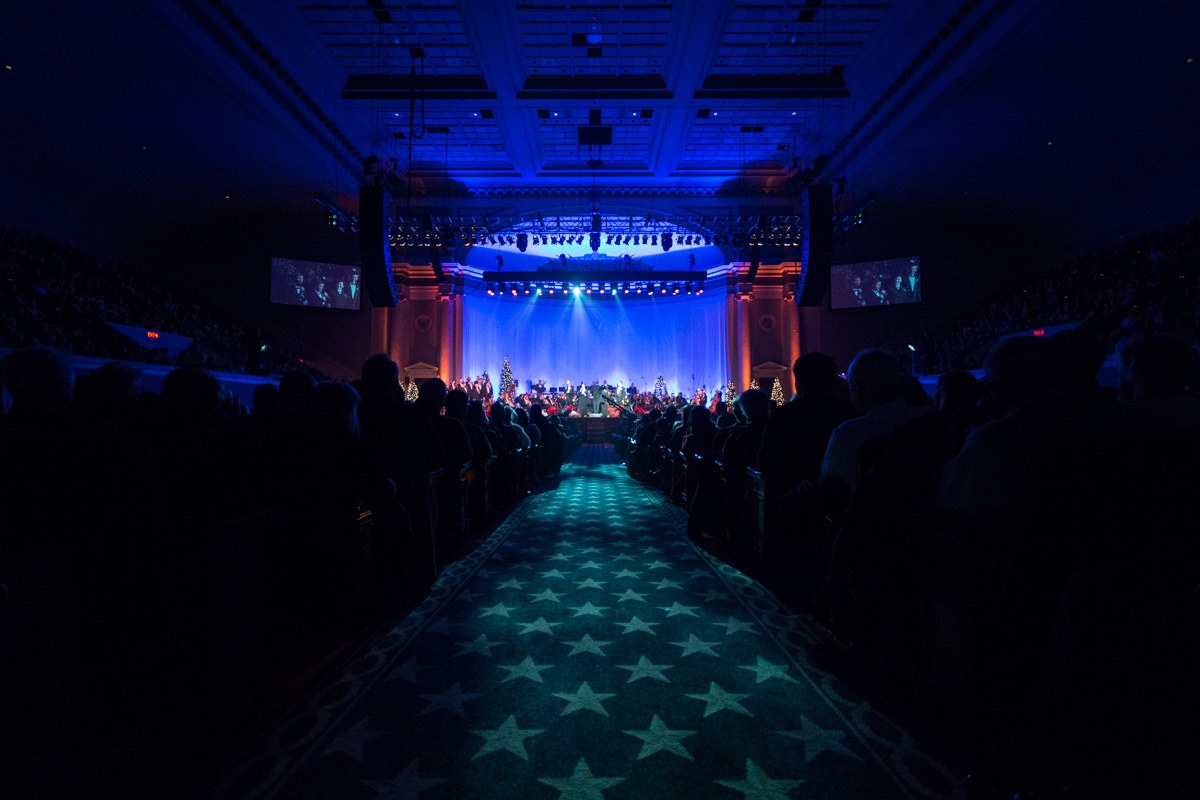 Ein großer Auditorium mit sitzenden Zuschauern, eine Bühne mit Musikern und über Kopfbeleuchtung und Fernseher, was auf einen Konzertsaal während der 2019 National Convention hinweist.