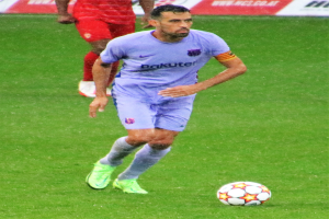 Ein Fußballer in Sportkleidung und -schuhen ist im Einsatz auf dem Feld, mit einer Texttafel im Hintergrund.