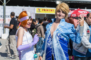 Ein Junge und ein Mädchen in Kostümen stehen in der Mitte des Bildes, mit anderen Menschen und Plakaten im Hintergrund.