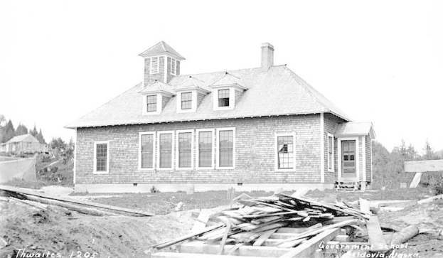 Schwarzes und weißes Foto eines Regierungsgebäudes aus dem Jahr 1905, umgeben von Bäumen unter einem klaren Himmel, mit Holzplanken und der Beschriftung "Regierungsgebäude, Thwaites, 1905" unten.