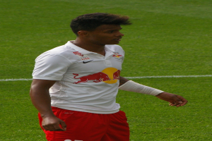 Ein Mann in weißem Hemd und roter Hose steht auf einem Fußballfeld und schaut rechts mit entschlossener Miene, er scheint ein Flügelstürmer zu sein.