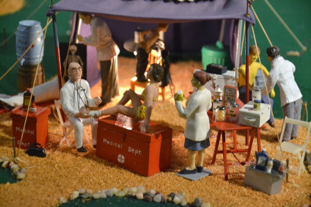 Eine Sammlung von Spielzeugen auf einem Tisch mit einer medizinisch thematisierten Schachtel, einem violetten Zelt und verstreuten Gegenständen im Hintergrund.